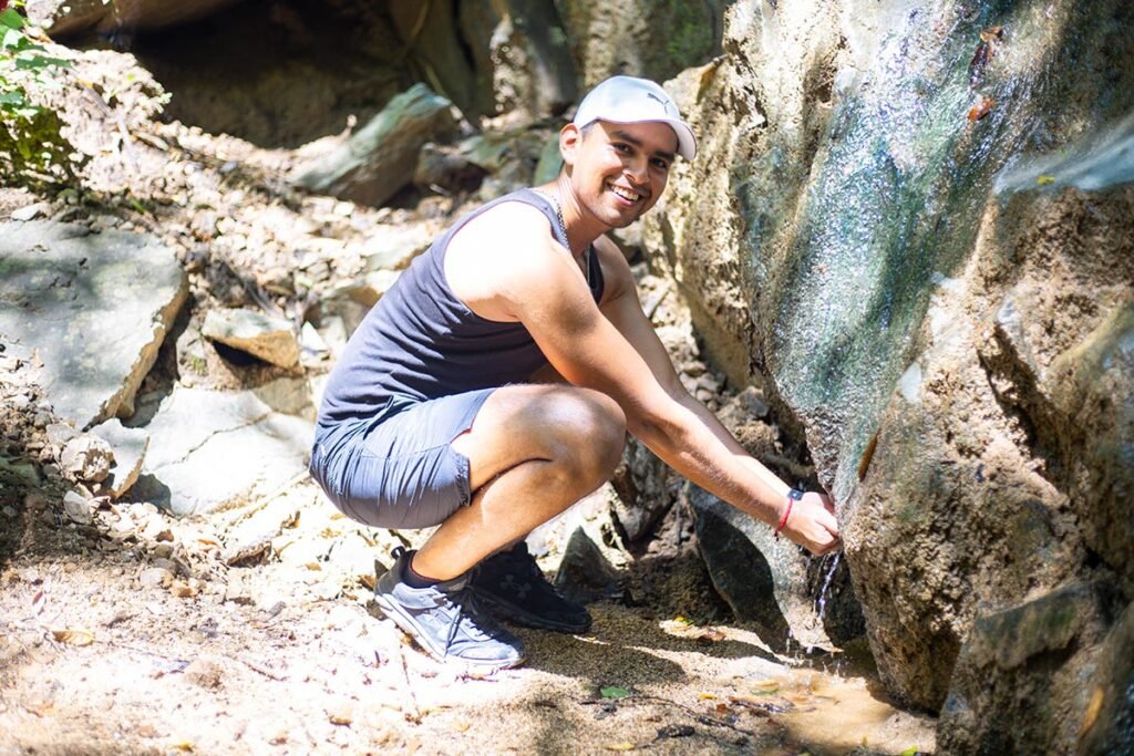 Tour Hiking Jorullo Point 3 Turista refrescándose en un pequeño arroyo de agua cristalina durante su recorrido de senderismo en la montaña.