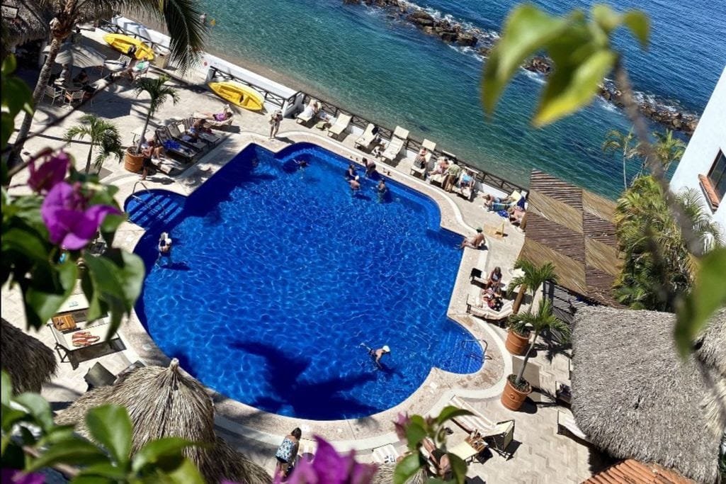 Alberca principal con vista al mar y palapas en el Costa Sur Resort Puerto Vallarta.