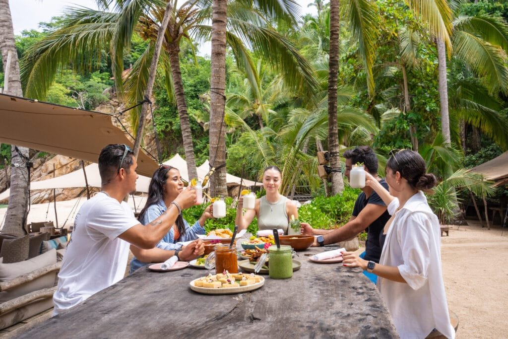 Grupo de amigos brindando en la playa Majahuitas con bebidas tropicales.
