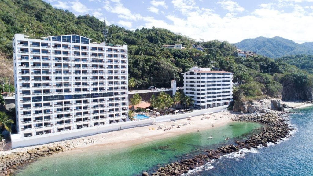 Fachada del Costa Sur Resort Puerto Vallarta con vista a la playa y montaña en segundo plano.