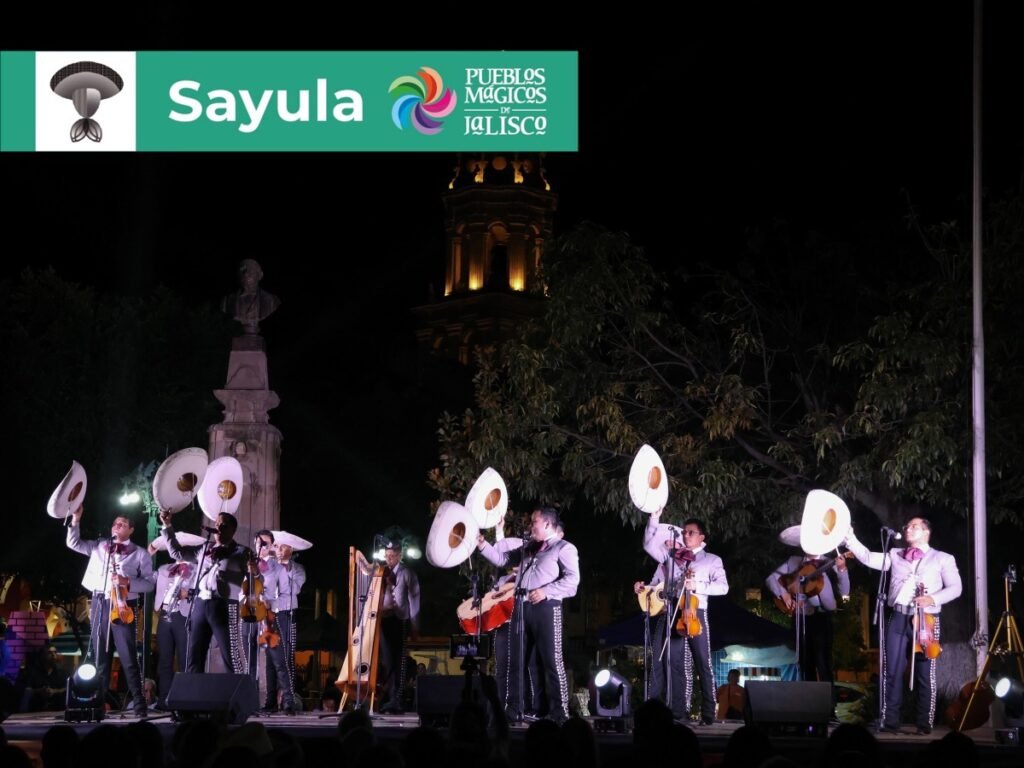 Encuentro Internacional del Mariachi y la Charrería 2026: Sedes 2 Integrantes de mariachi alzando sus sombreros charros blancos en concierto nocturno en el Pueblo Mágico de Sayula, Jalisco.