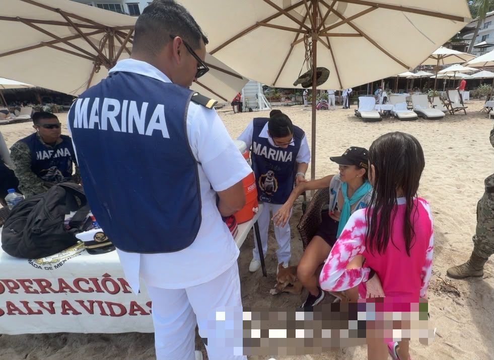 Operación Salvavidas Verano 2026: Éxito Total en Playas 2 Médico de Sanidad Naval revisando el brazo de una turista bajo sombrilla de playa en el módulo de la Operación Salvavidas de Puerto Vallarta.