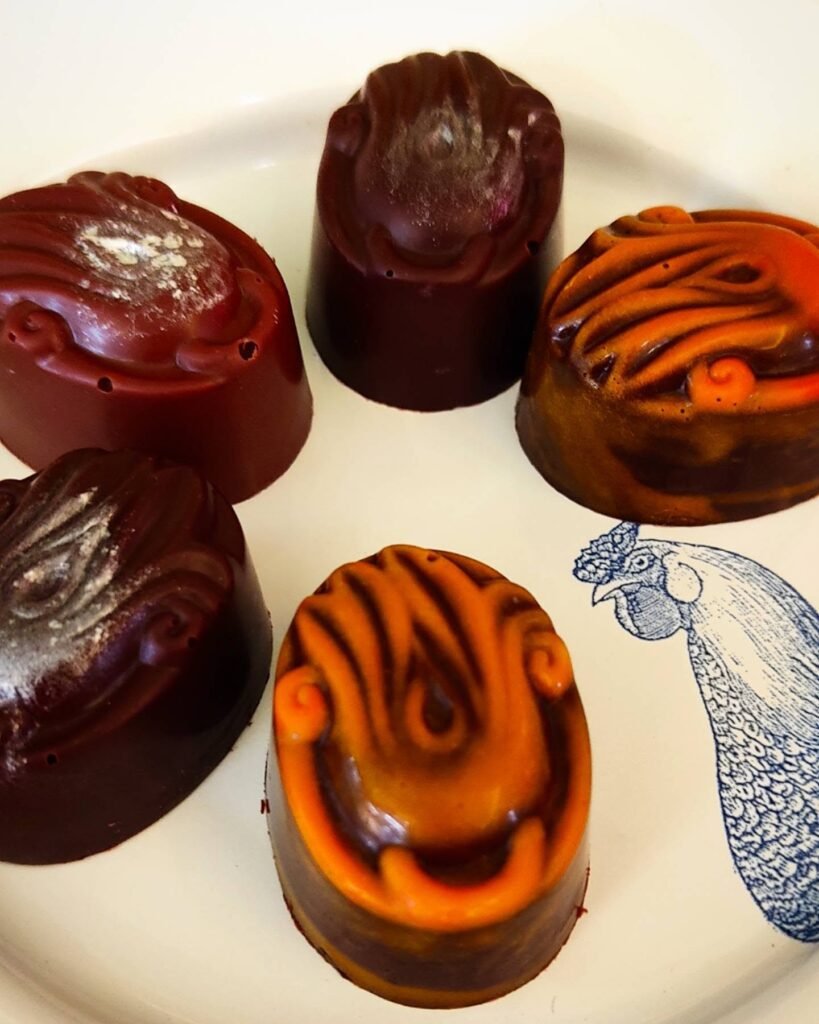 Día Internacional del Chocolate en Jalisco 2026: Rutas Top 3 Plato de porcelana con cinco bombones de chocolate oscuro y naranja decorados a mano en el taller boutique Villa Cocoa en San Sebastián del Oeste.