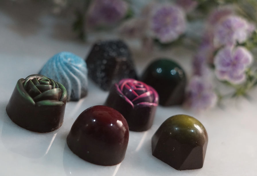 Día Internacional del Chocolate en Jalisco 2026: Rutas Top 5 Selección de finos bombones de chocolate con brillo espejo en forma de rosas y gemas facetadas sobre superficie de mármol pulido.