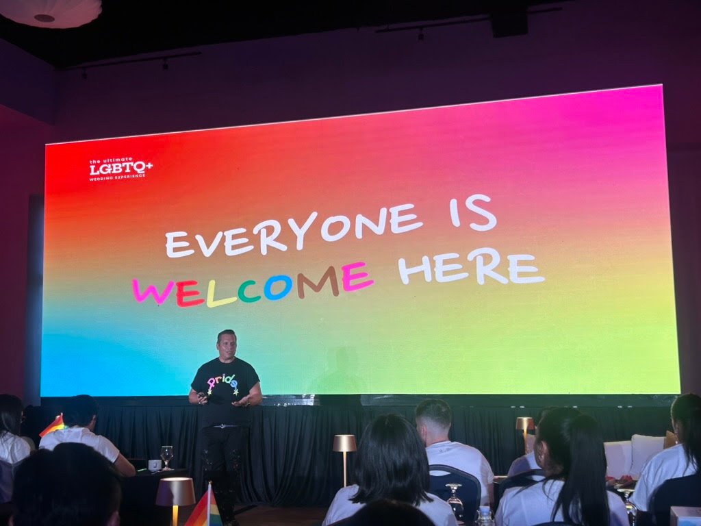 Bodas LGBTQ+ en Puerto Vallarta: certificación líder 3 Ponente frente a pantalla multicolor con el lema Everyone Is Welcome Here en la cumbre de turismo de romance diverso.