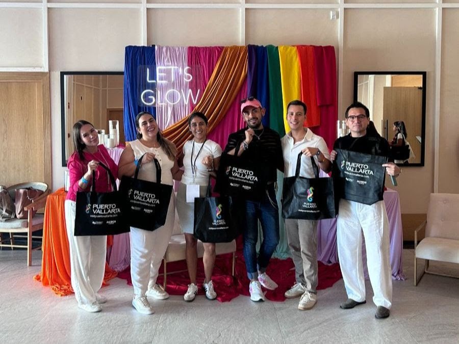 Bodas LGBTQ+ en Puerto Vallarta: certificación líder 4 Comitiva y organizadores sosteniendo bolsas de Puerto Vallarta frente a fondo arcoíris en The Ultimate LGBTQ+ Wedding Experience.