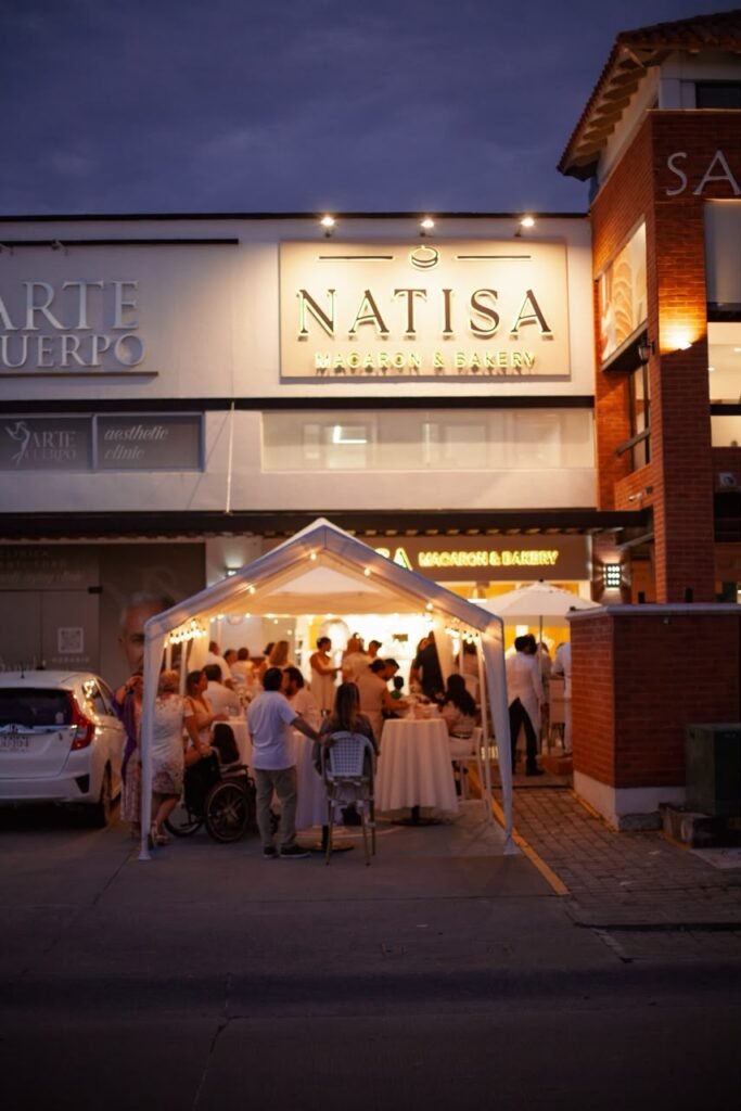 Vista nocturna de la fachada de Natisa en Plaza San Marino durante el cóctel de inauguración con invitados y ambiente acogedor en Fluvial Vallarta.
