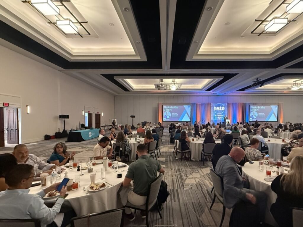 Gran salón con más de 300 asesores de viajes de Arizona en mesas redondas escuchando presentaciones.