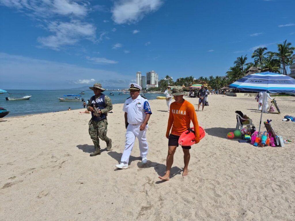 Operación Salvavidas Verano 2026: Éxito Total en Playas 4 Oficial de marina, infante y salvavidas naval caminando en la arena dorada de Playa Los Muertos en Puerto Vallarta junto a los bañistas.
