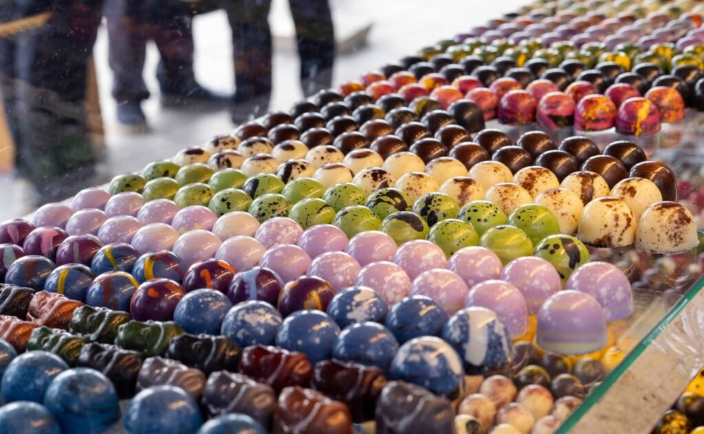Día Internacional del Chocolate en Jalisco 2026: Rutas Top 4 Vitrina de exhibición con filas ordenadas de bombones de chocolate brillantes pintados a mano en tonos pasteles para catas gourmet.